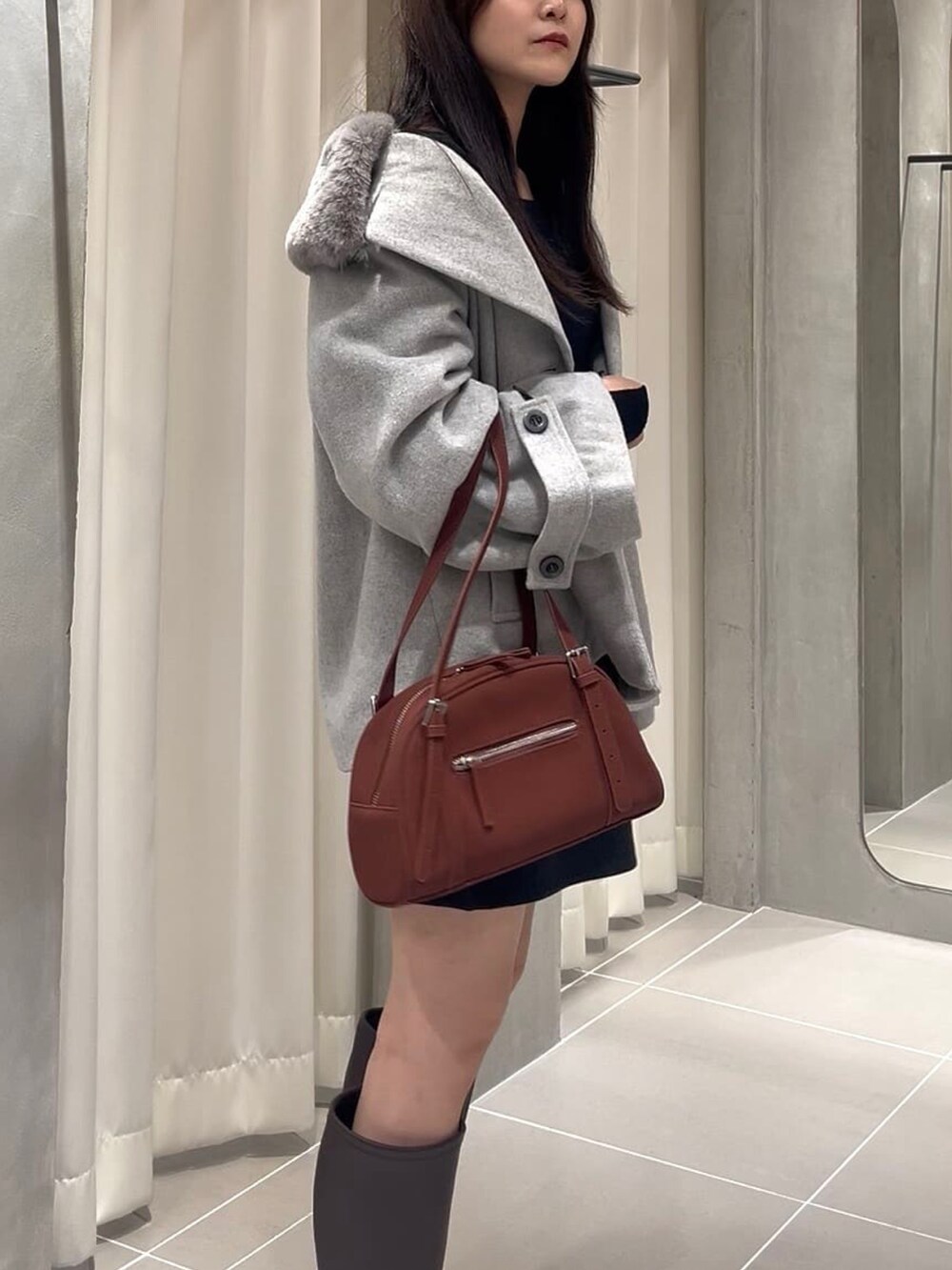 グレー系のピーコート、ブラック系のスカート、ブラック系のブーツを着用したレディースの秋コーディネートの3枚目の写真