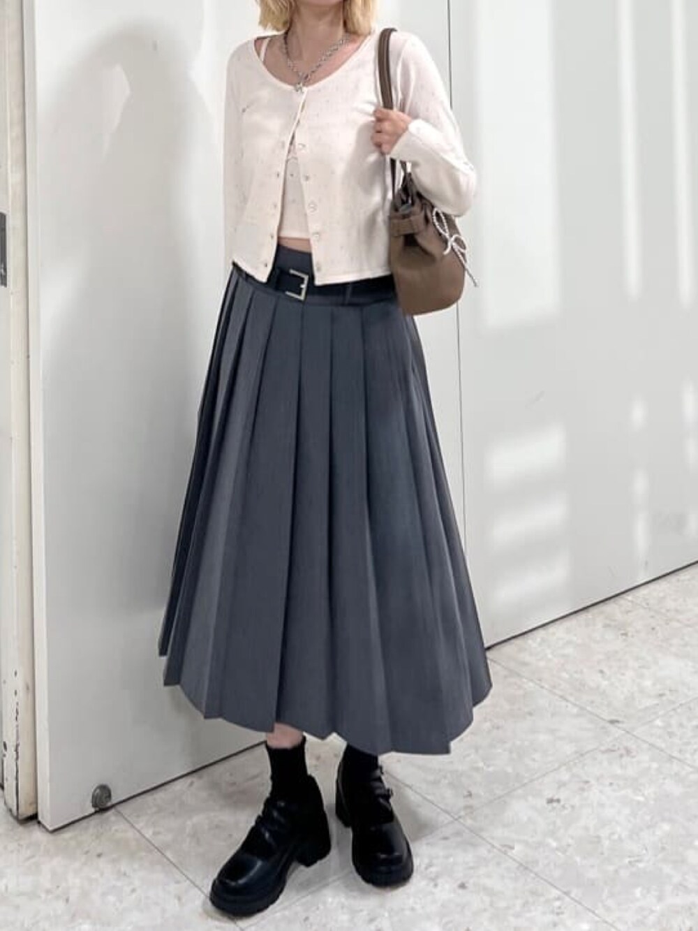 グレー系のスカート、ホワイト系のアンサンブル、ブラウン系のショルダーバッグを着用したレディースの夏コーディネートの2枚目の写真