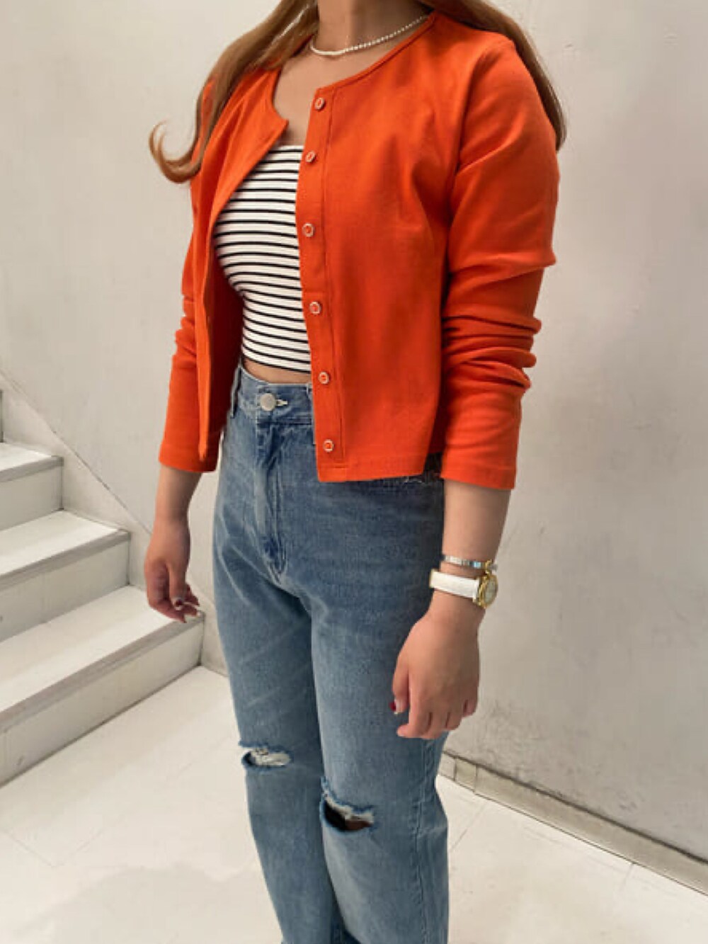 オレンジ系のカーディガン/ボレロ、ホワイト系のキャミソール、ブルー系のデニムパンツを着用したレディースの春コーディネートの3枚目の写真