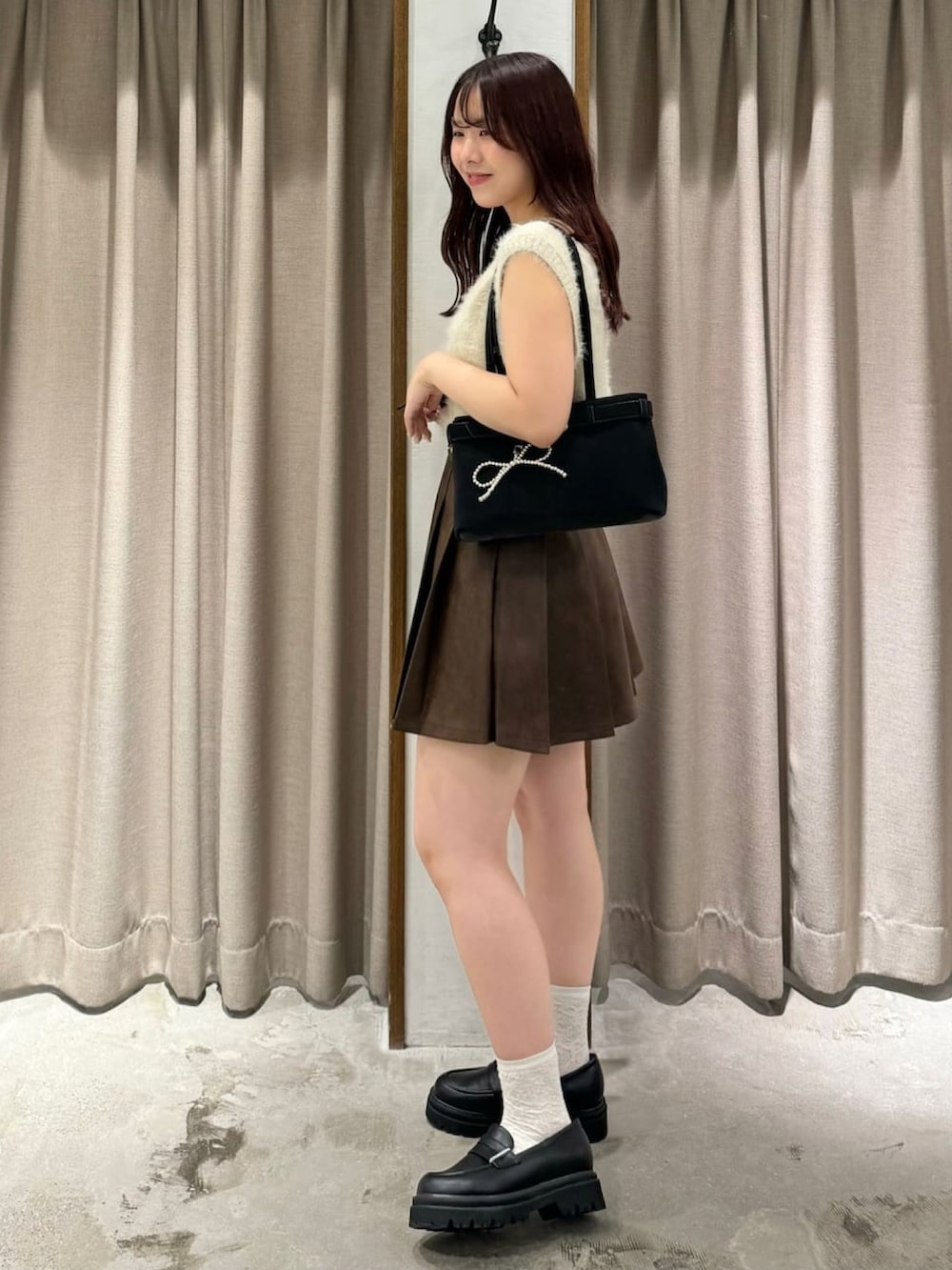 ホワイト系のベスト、ブラウン系のスカート、ブラック系のローファーを着用したレディースの秋コーディネートの2枚目の写真