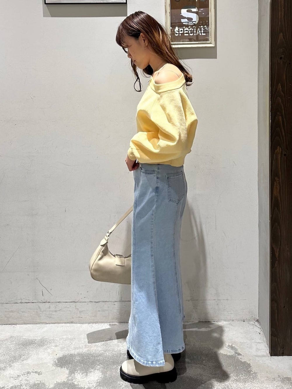 イエロー系のニット/セーター、ブルー系のデニムスカート、ホワイト系のショルダーバッグを着用したレディースの冬コーディネートの2枚目の写真