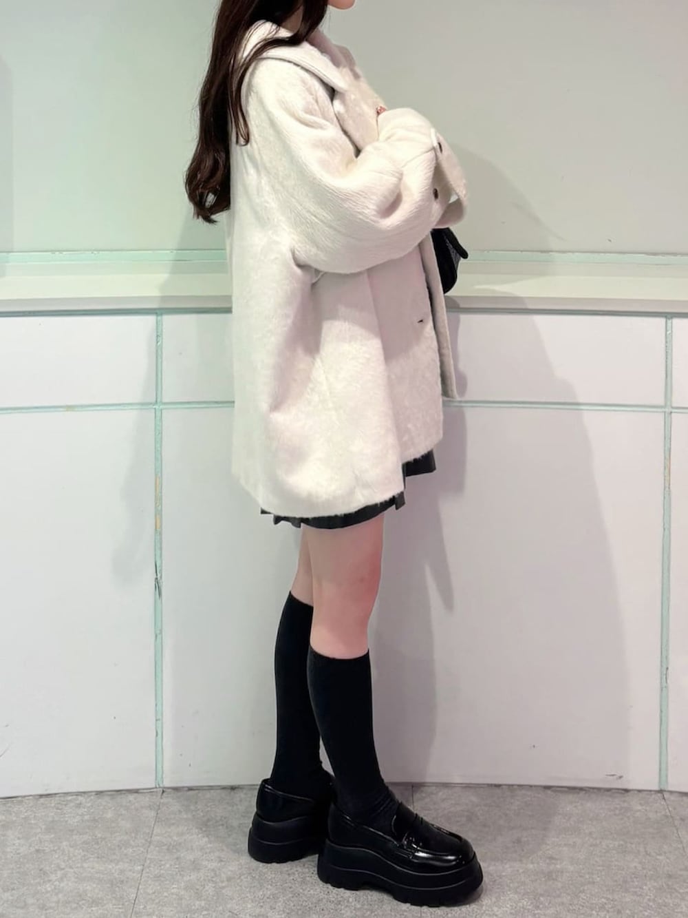 ホワイト系のチェスターコート、グレー系のスカート、ブルー系のニット/セーターを着用したレディースの秋コーディネートの3枚目の写真