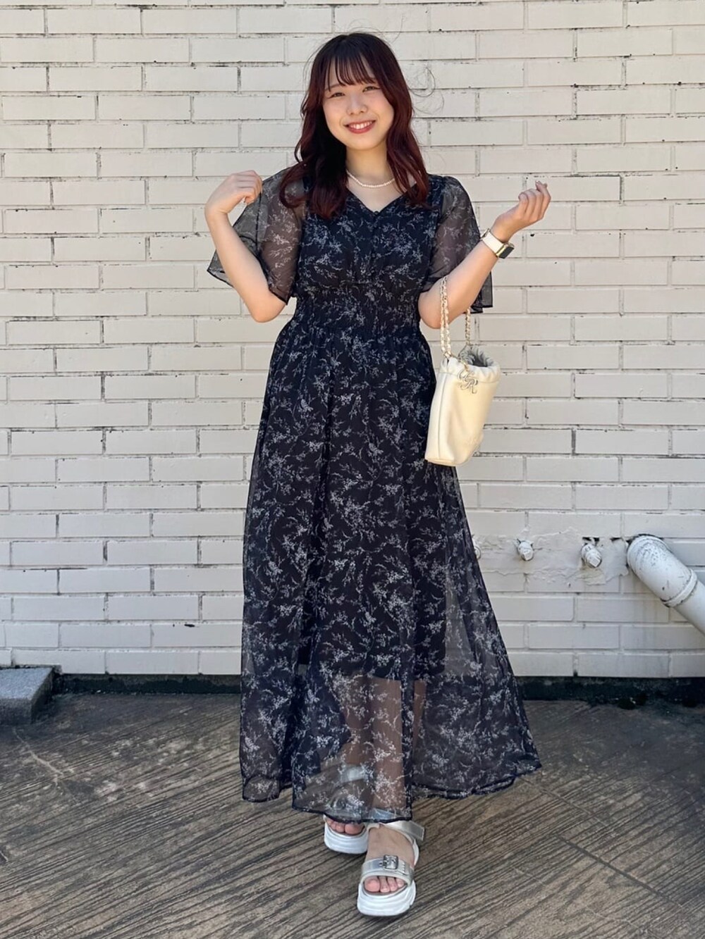 ブラック系のワンピース、ブラック系のサンダル、ホワイト系のハンドバッグを着用したレディースの夏コーディネートの2枚目の写真