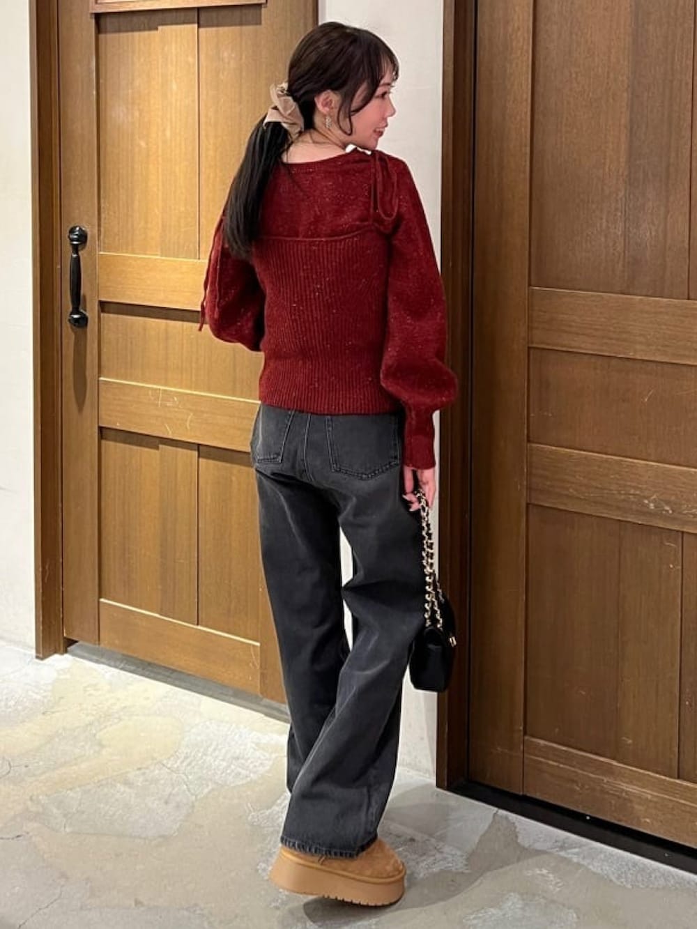 レッド系のニット/セーター、ブラック系のデニムパンツ、ブラック系のショルダーバッグを着用したレディースの冬コーディネートの2枚目の写真