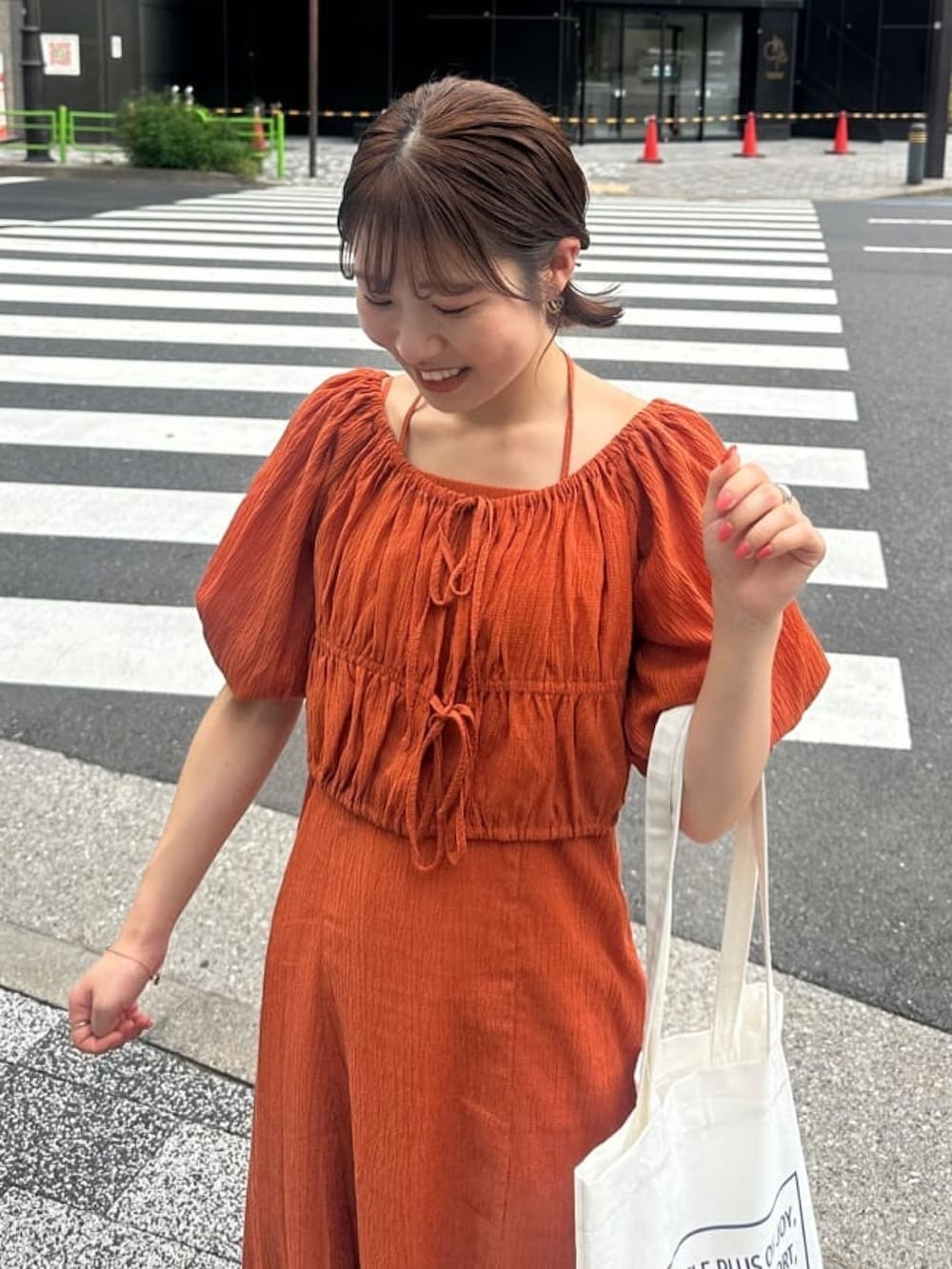 オレンジ系のワンピース、グレー系のサンダル、ホワイト系のトートバッグを着用したレディースの夏コーディネートの2枚目の写真