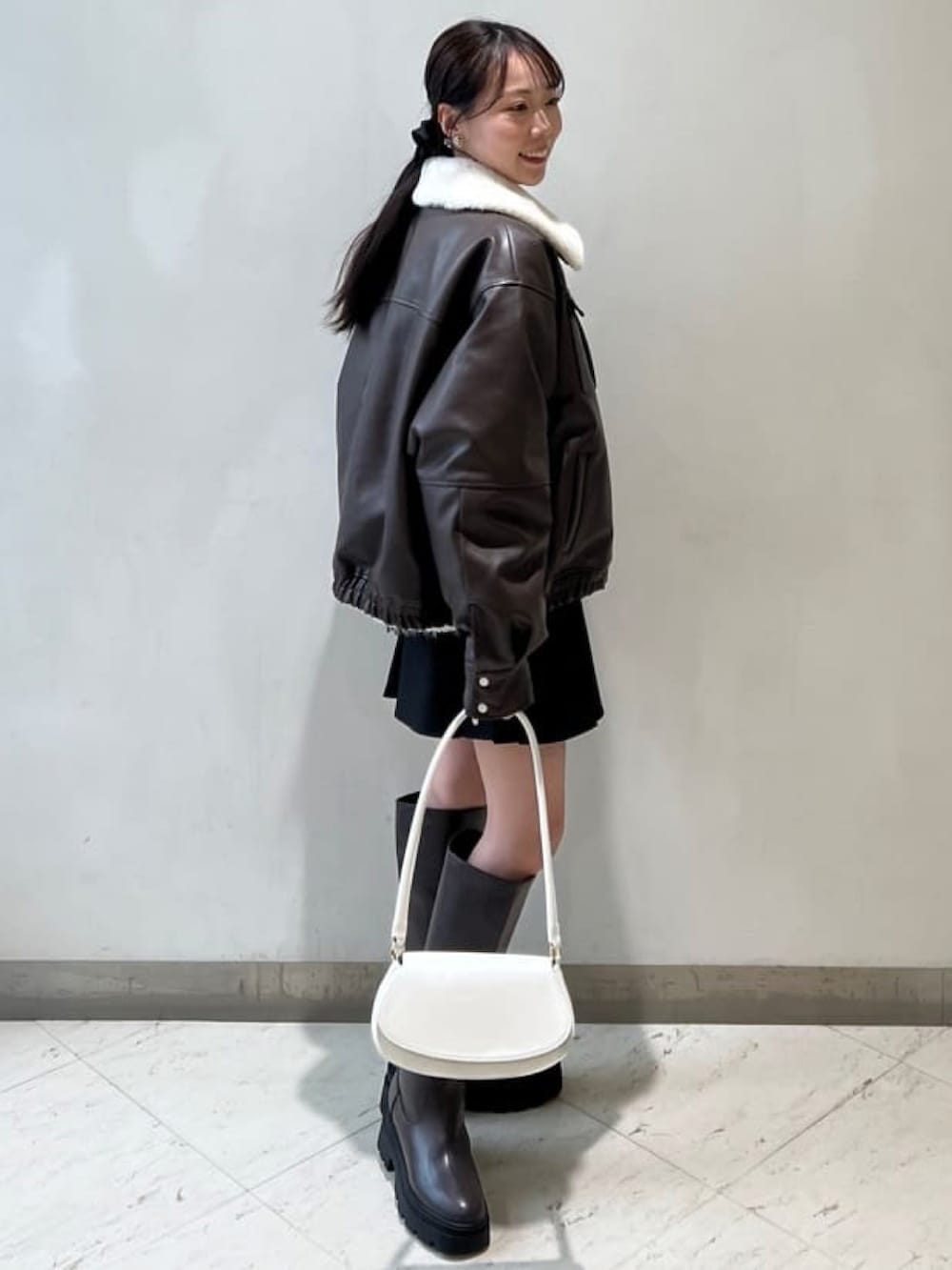 ブラウン系のブルゾン、ブラック系のスカート、ブラウン系のブーツを着用したレディースの冬コーディネートの2枚目の写真