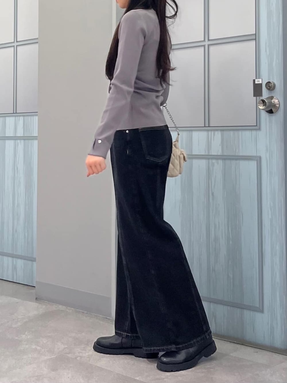 グレー系のニット/セーター、ブラック系のデニムパンツ、ホワイト系のショルダーバッグを着用したレディースの冬コーディネートの2枚目の写真