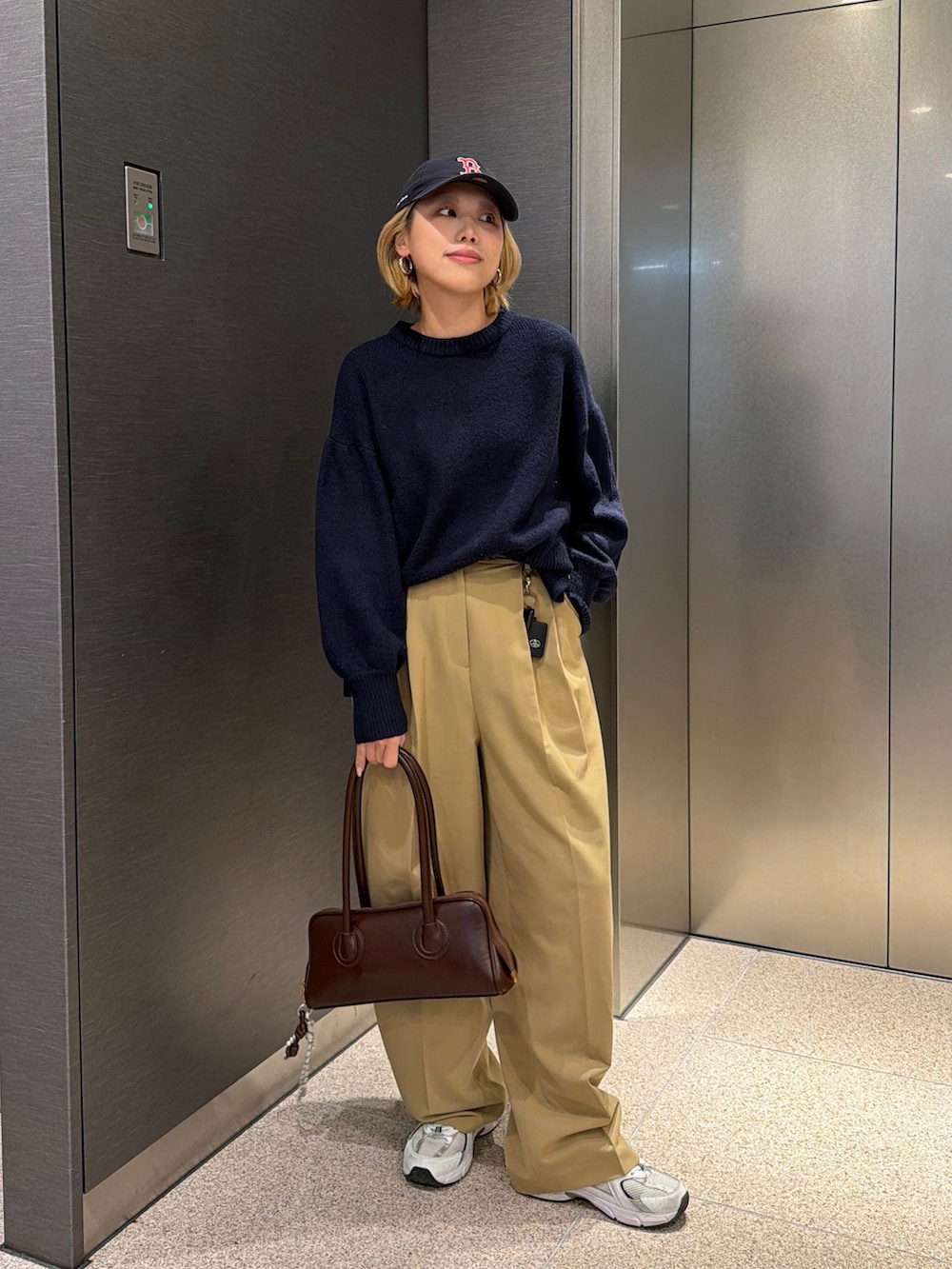 ベージュ系のスラックス、ブラウン系のボストンバッグ、ホワイト系のスニーカーを着用したレディースの冬コーディネートの3枚目の写真