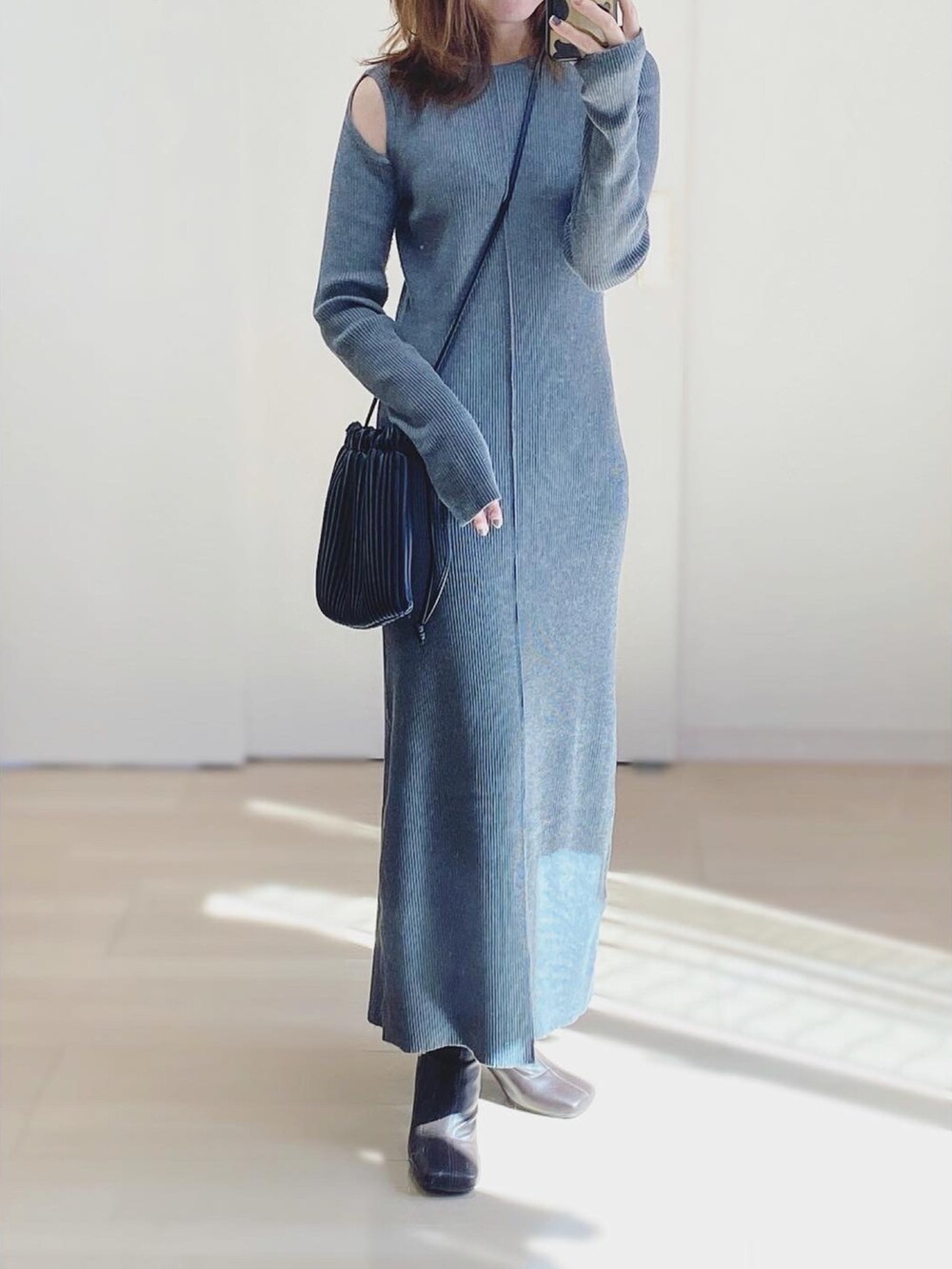 グレー系のワンピース、ブラウン系のブーツ、ブラック系のショルダーバッグを着用したレディースの秋コーディネートの2枚目の写真