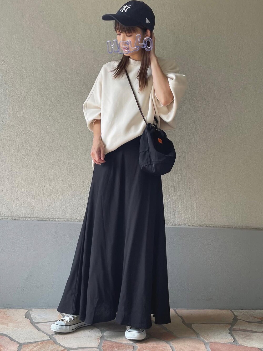 ブラック系のスカート、ベージュ系のスニーカー、ブルー系のキャップを着用したレディースの秋コーディネートの2枚目の写真