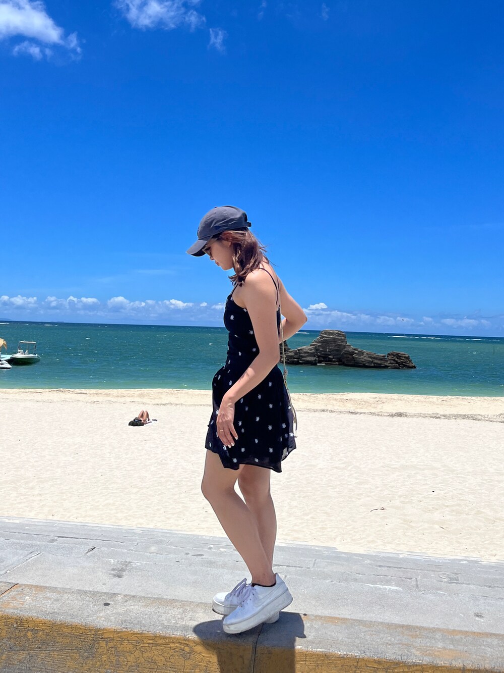 ブラック系のワンピース、ホワイト系のスニーカー、グレー系のキャップを着用したレディースの夏コーディネートの2枚目の写真