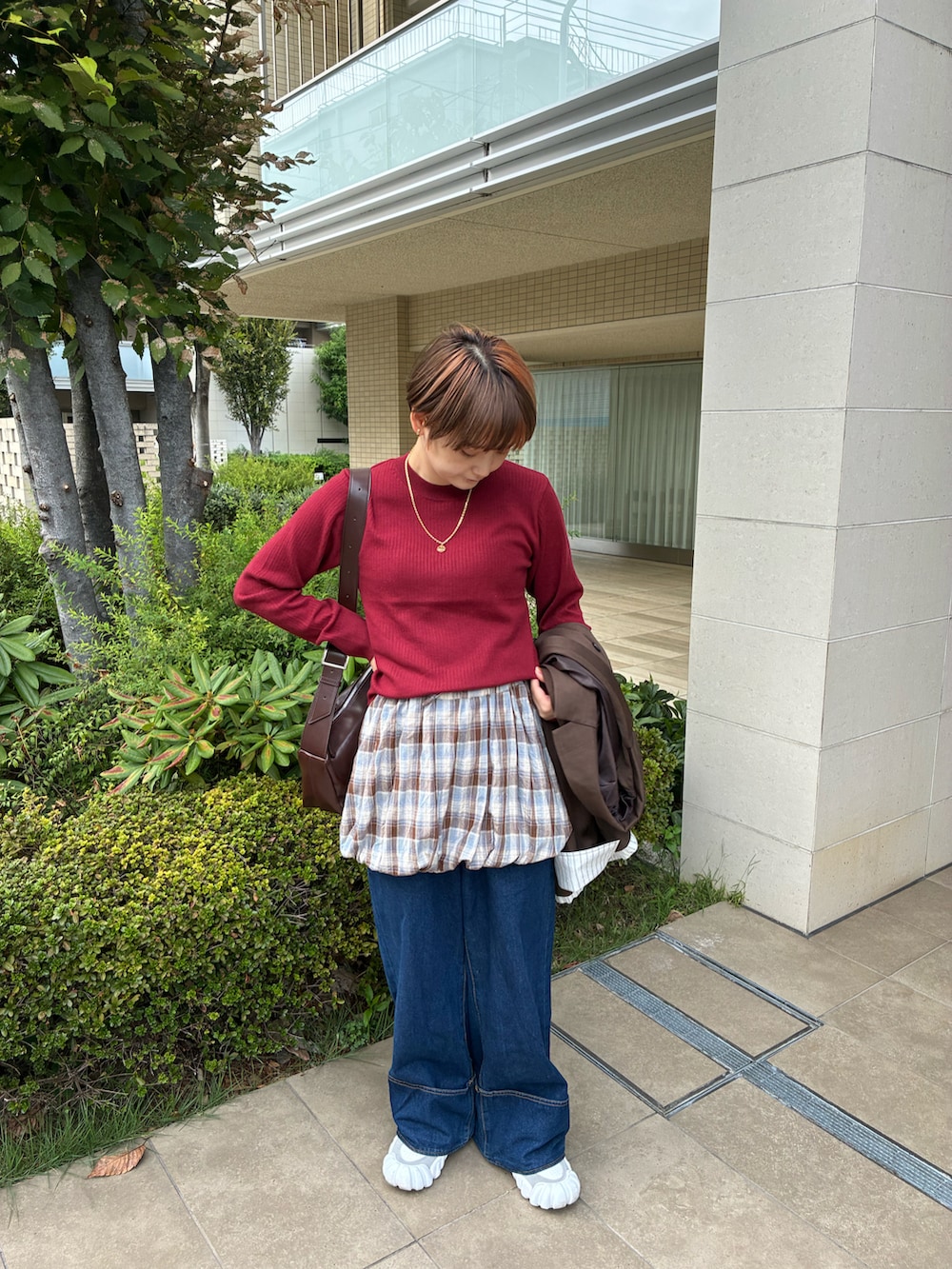 レッド系のニット/セーター、ブラウン系のスカート、ブルー系のデニムパンツを着用したレディースの秋コーディネートの3枚目の写真