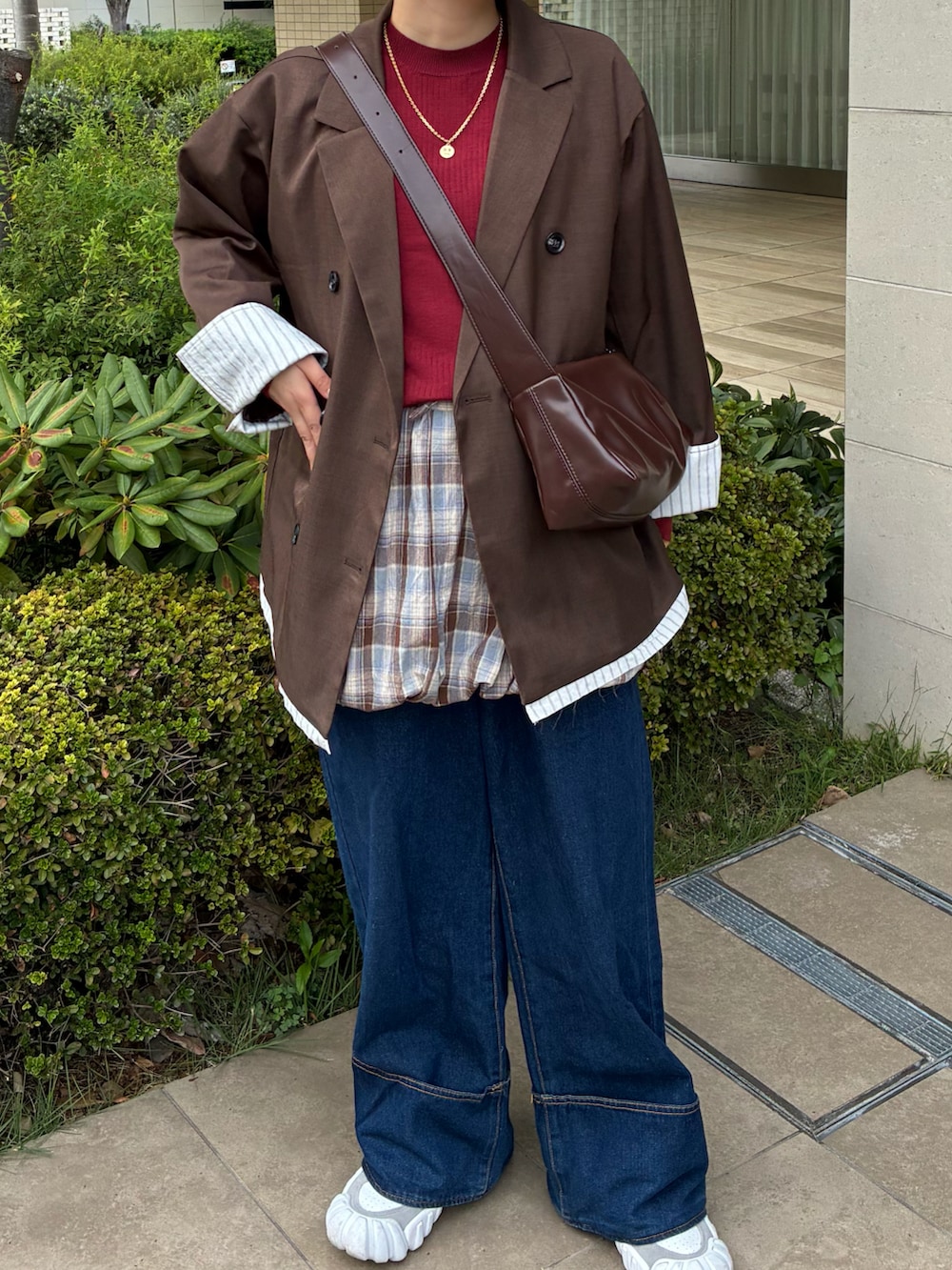 レッド系のニット/セーター、ブラウン系のスカート、ブルー系のデニムパンツを着用したレディースの秋コーディネートの5枚目の写真