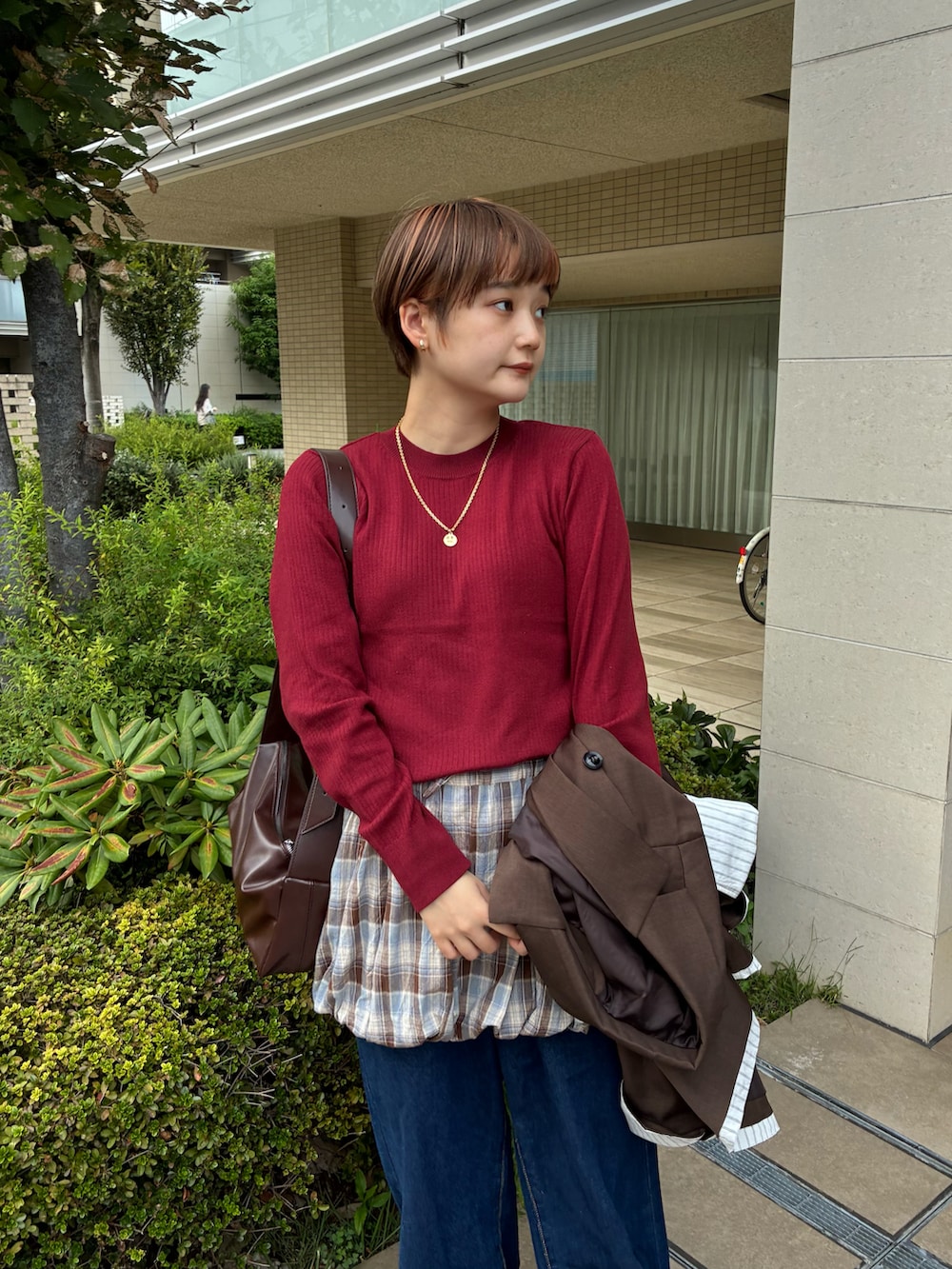 レッド系のニット/セーター、ブラウン系のスカート、ブルー系のデニムパンツを着用したレディースの秋コーディネートの4枚目の写真