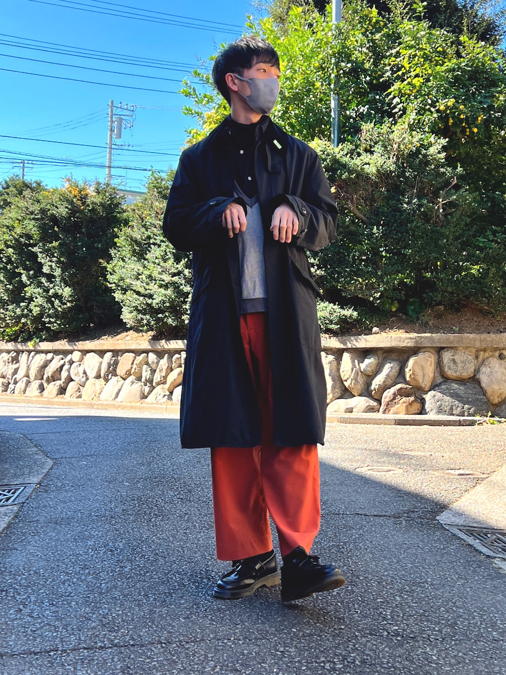 ブラック系のステンカラーコート、グレー系のニット/セーター、オレンジ系のスラックスを着用したメンズの秋コーディネートの3枚目の写真