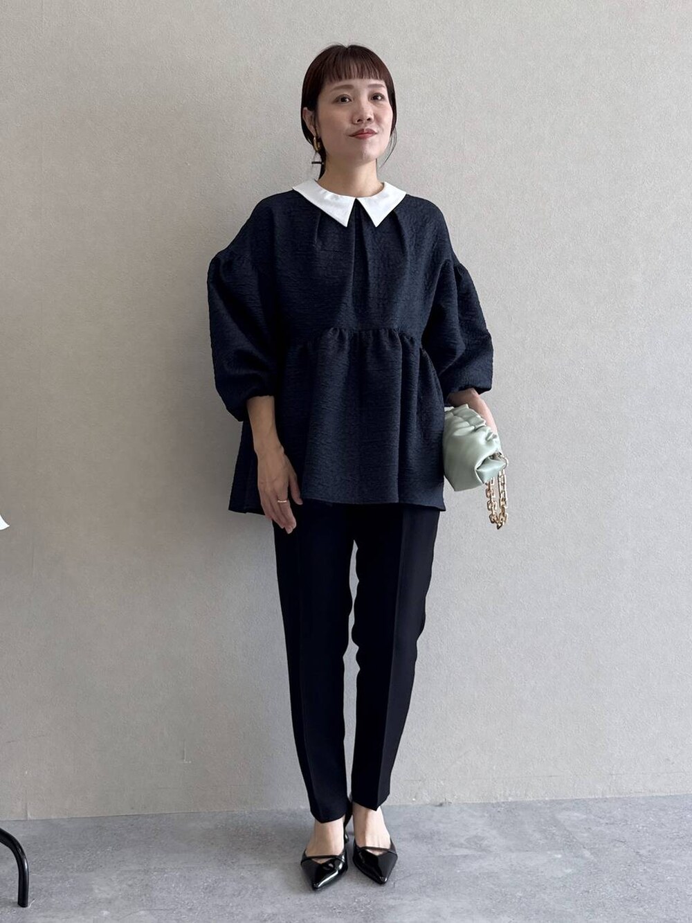 ブラック系のパンプス、グリーン系のショルダーバッグ、ブルー系のパンツドレスを着用したレディースの冬コーディネートの7枚目の写真