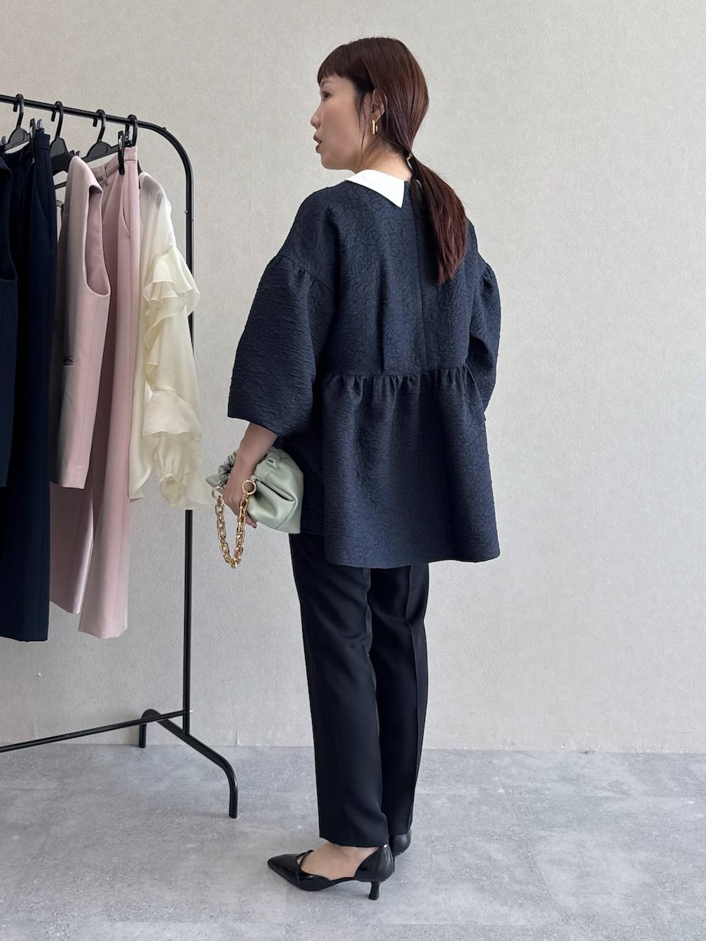 ブラック系のパンプス、グリーン系のショルダーバッグ、ブルー系のパンツドレスを着用したレディースの冬コーディネートの4枚目の写真