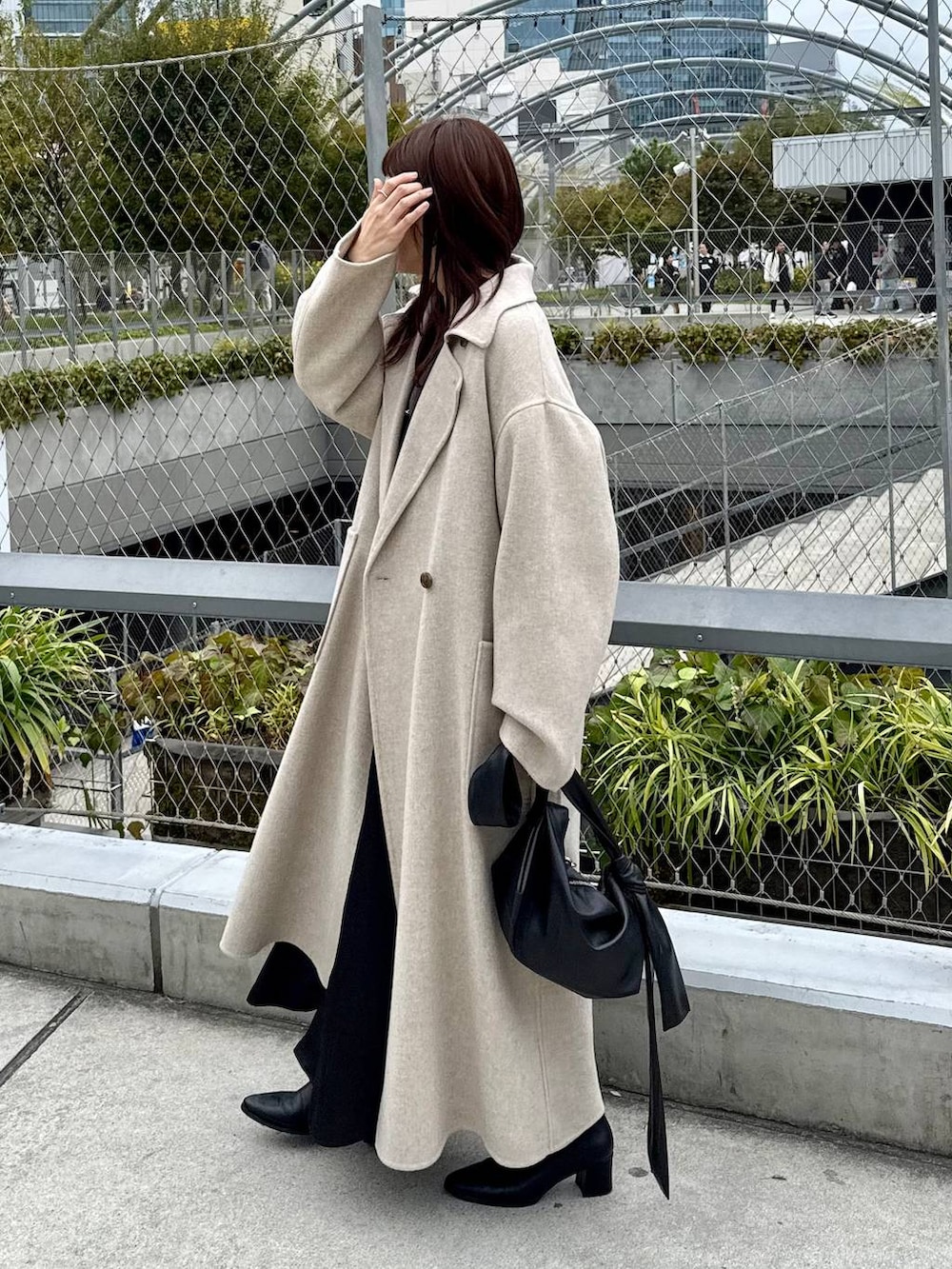 ベージュ系のステンカラーコート、ブラック系のブーツ、グレー系のカーディガン/ボレロを着用したレディースの秋コーディネートの2枚目の写真