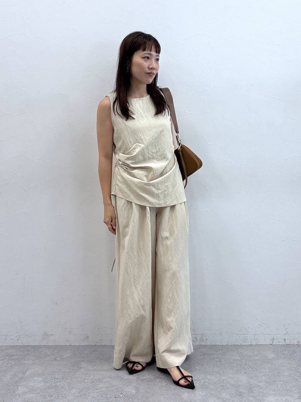 イエロー系のショルダーバッグ、ベージュ系のパンツドレスを着用したレディースの夏コーディネートの2枚目の写真