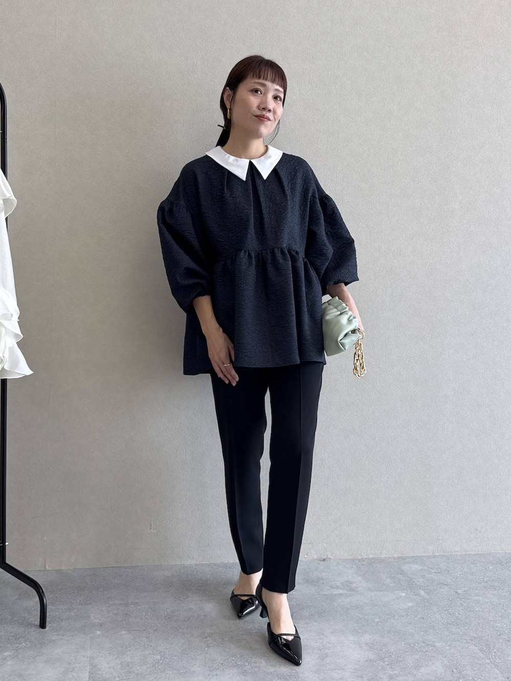 ブラック系のパンプス、グリーン系のショルダーバッグ、ブルー系のパンツドレスを着用したレディースの冬コーディネートの2枚目の写真