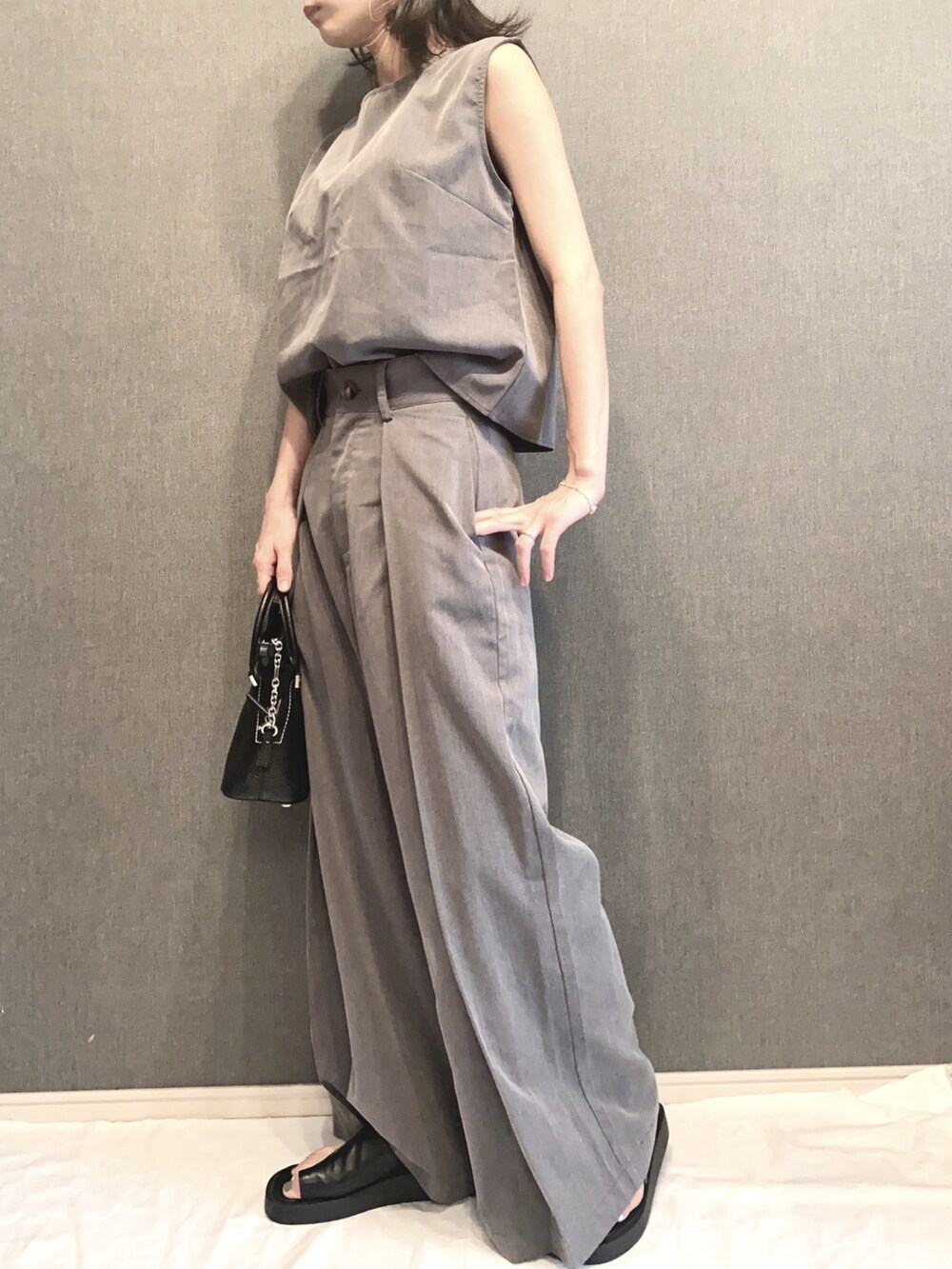 グレー系のセットアップ、ブラック系のショルダーバッグ、ブラック系のサンダルを着用したレディースの夏コーディネートの2枚目の写真