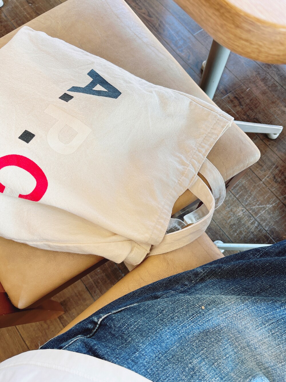 ホワイト系のトートバッグ、ブルー系のデニムパンツ、ブラック系のスニーカーを着用したレディースの秋コーディネートの2枚目の写真