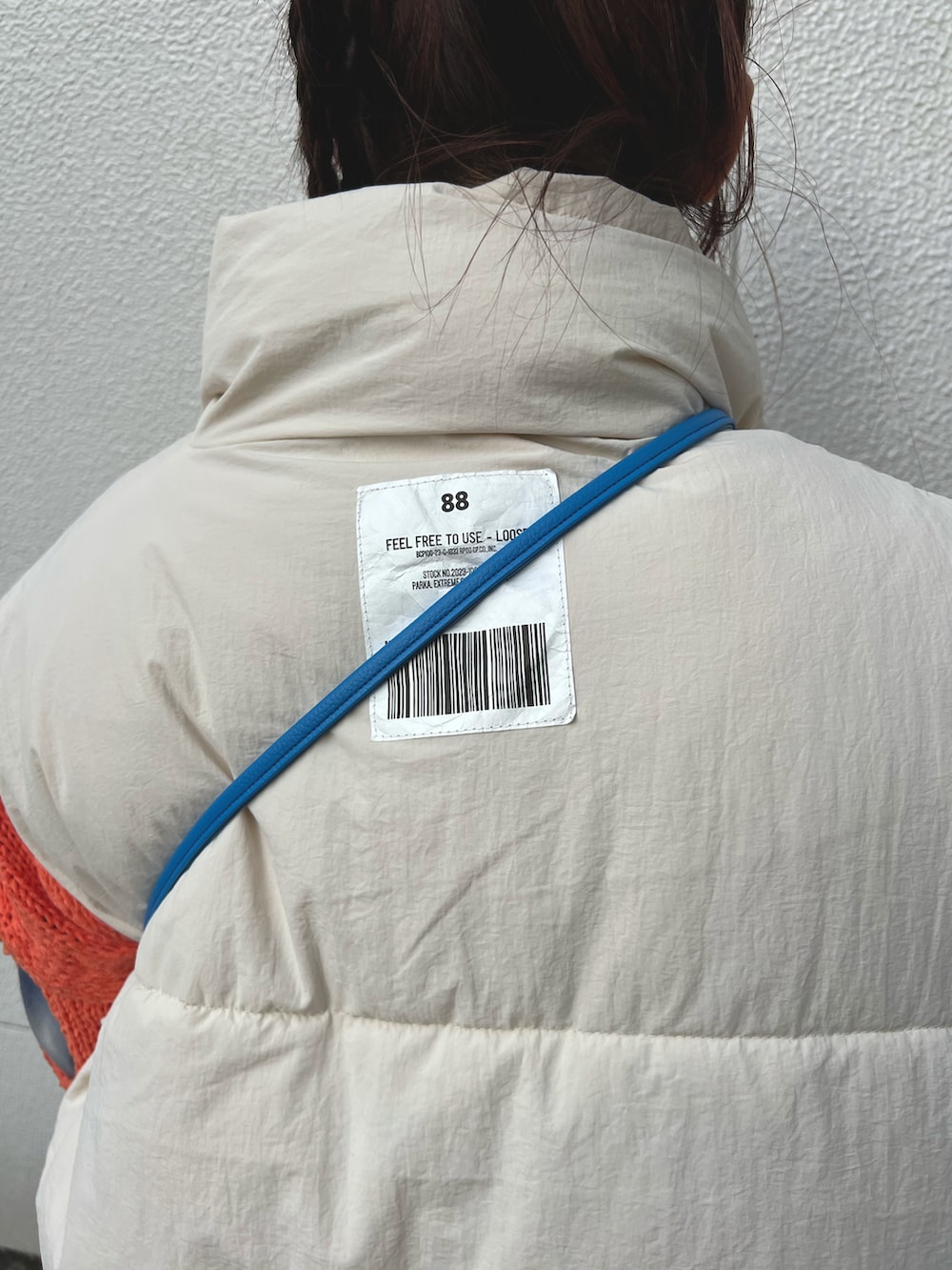 ホワイト系のダウンベスト、オレンジ系のニット/セーター、シルバー系のショルダーバッグを着用したレディースの秋コーディネートの4枚目の写真