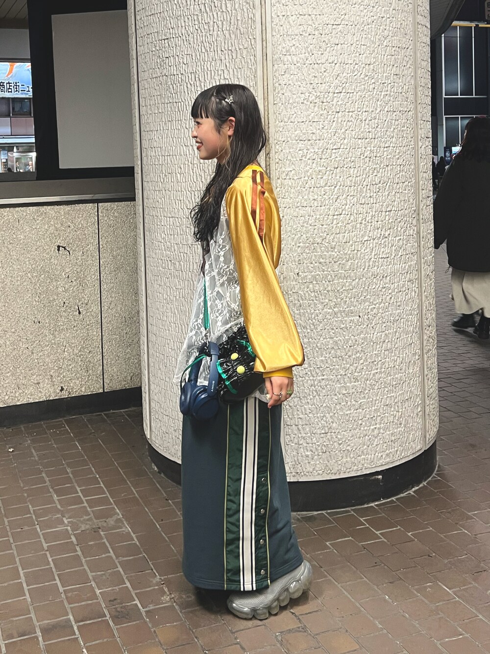 グリーン系のスカート、ブラック系のショルダーバッグ、イエロー系のTシャツ/カットソーを着用したレディースの冬コーディネートの2枚目の写真