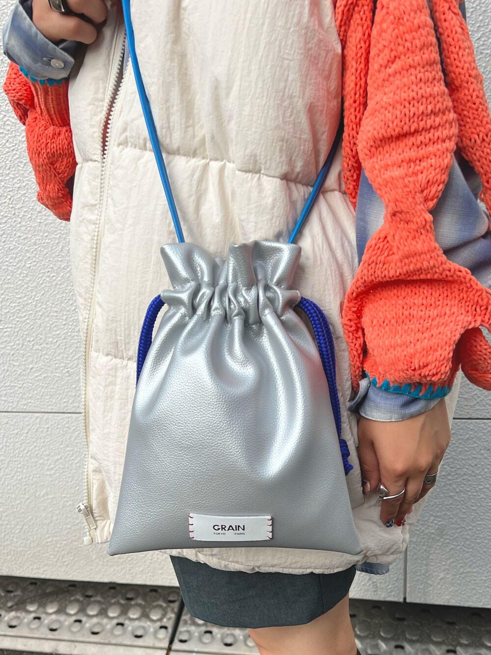 ホワイト系のダウンベスト、オレンジ系のニット/セーター、シルバー系のショルダーバッグを着用したレディースの秋コーディネートの5枚目の写真