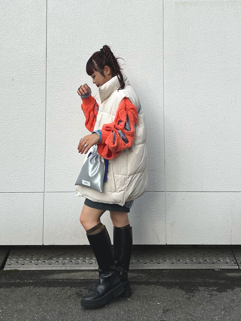 ホワイト系のダウンベスト、オレンジ系のニット/セーター、シルバー系のショルダーバッグを着用したレディースの秋コーディネートの2枚目の写真