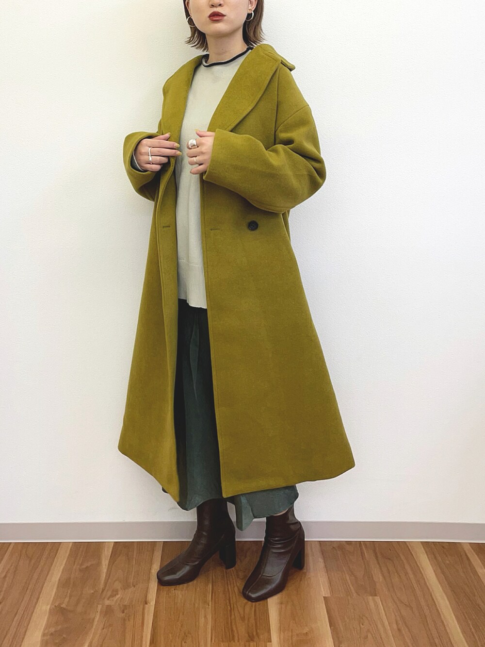 イエロー系のチェスターコート、ホワイト系のニット/セーター、ブルー系のスカートを着用したレディースの冬コーディネートの2枚目の写真