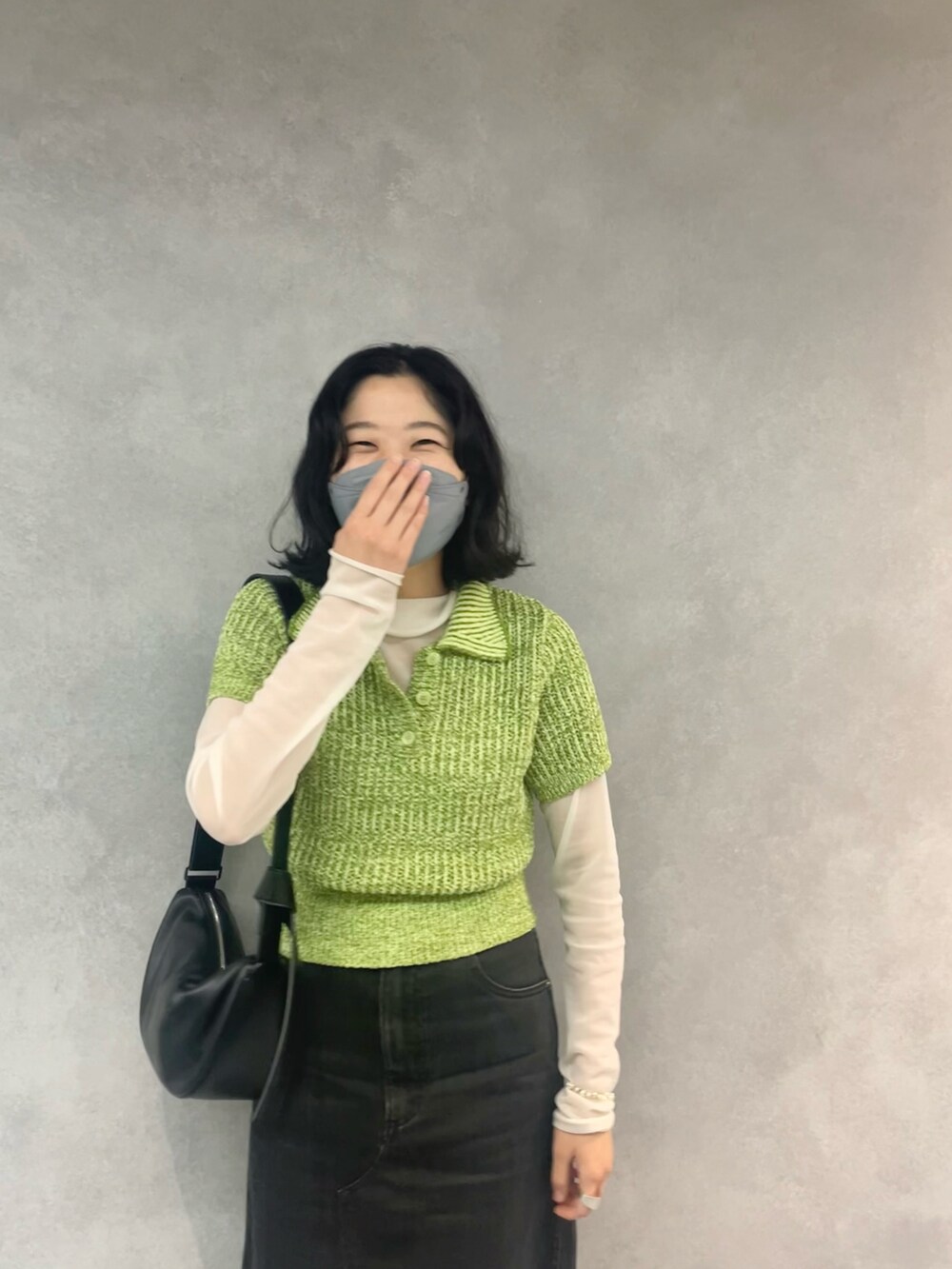 ブラック系のデニムスカート、グリーン系のニット/セーター、ブラック系のショルダーバッグを着用したレディースの春コーディネートの3枚目の写真