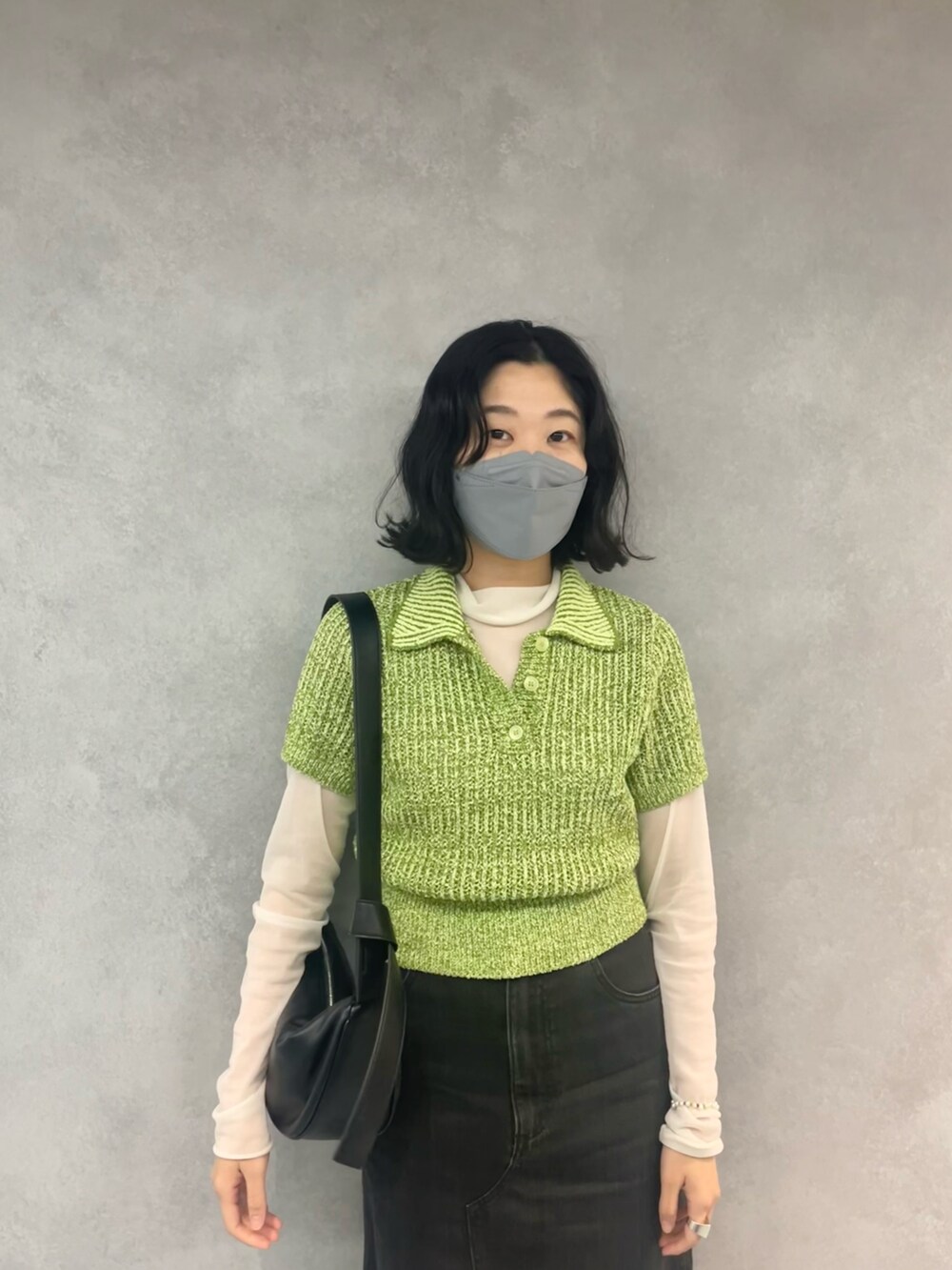 ブラック系のデニムスカート、グリーン系のニット/セーター、ブラック系のショルダーバッグを着用したレディースの春コーディネートの2枚目の写真