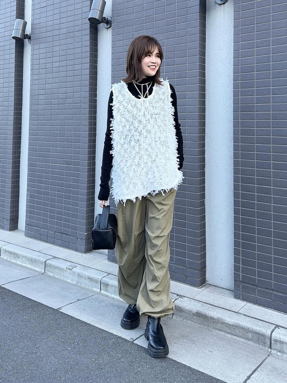 ホワイト系のトップス、グリーン系のパンツ、ブラック系のハンドバッグを着用したレディースの冬コーディネートの2枚目の写真