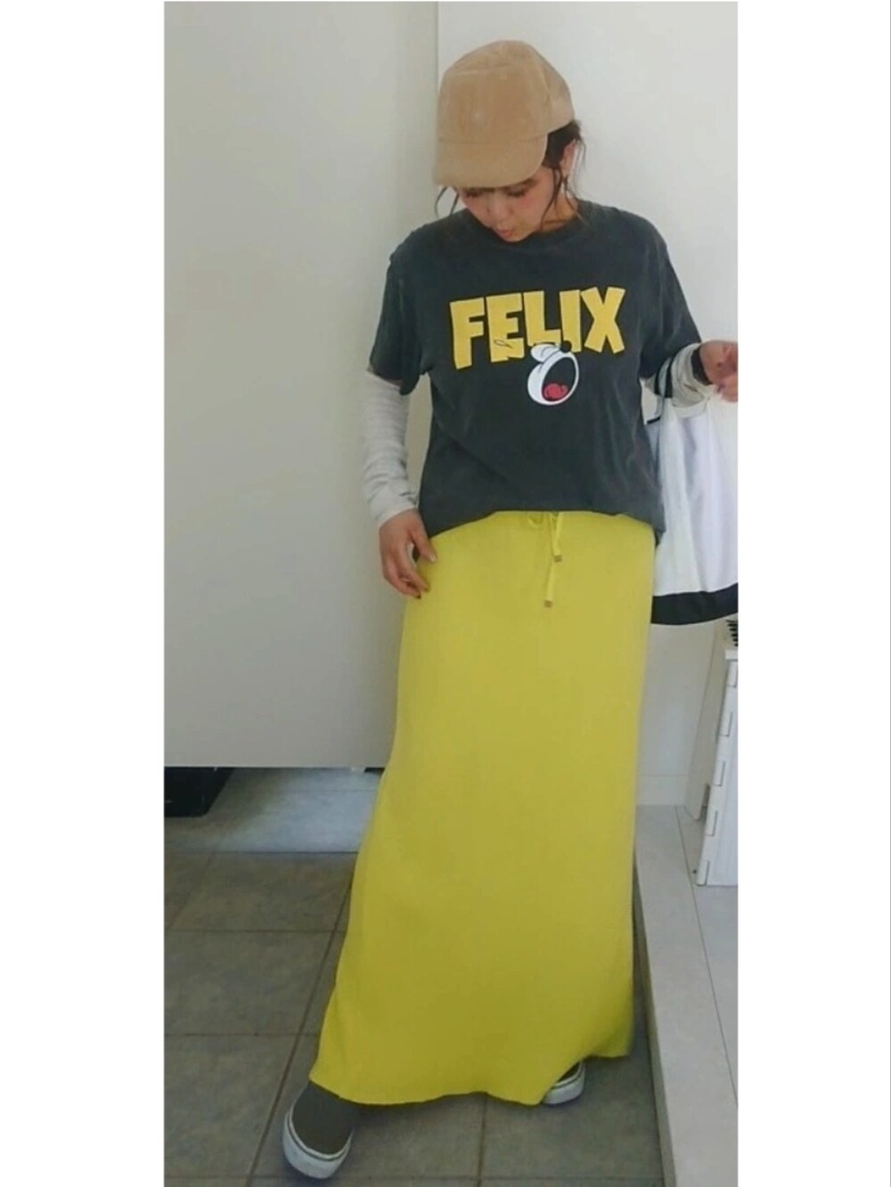 ブラック系のTシャツ/カットソー、イエロー系のスカート、ベージュ系のキャップを着用したレディースの秋コーディネートの4枚目の写真