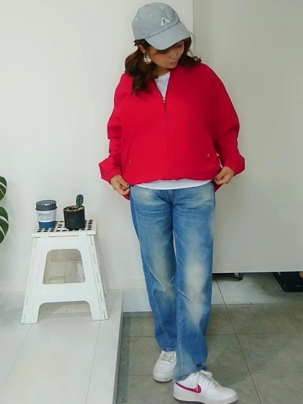 レッド系のブルゾン、ブルー系のデニムパンツ、ホワイト系のスニーカーを着用したレディースの秋コーディネートの2枚目の写真