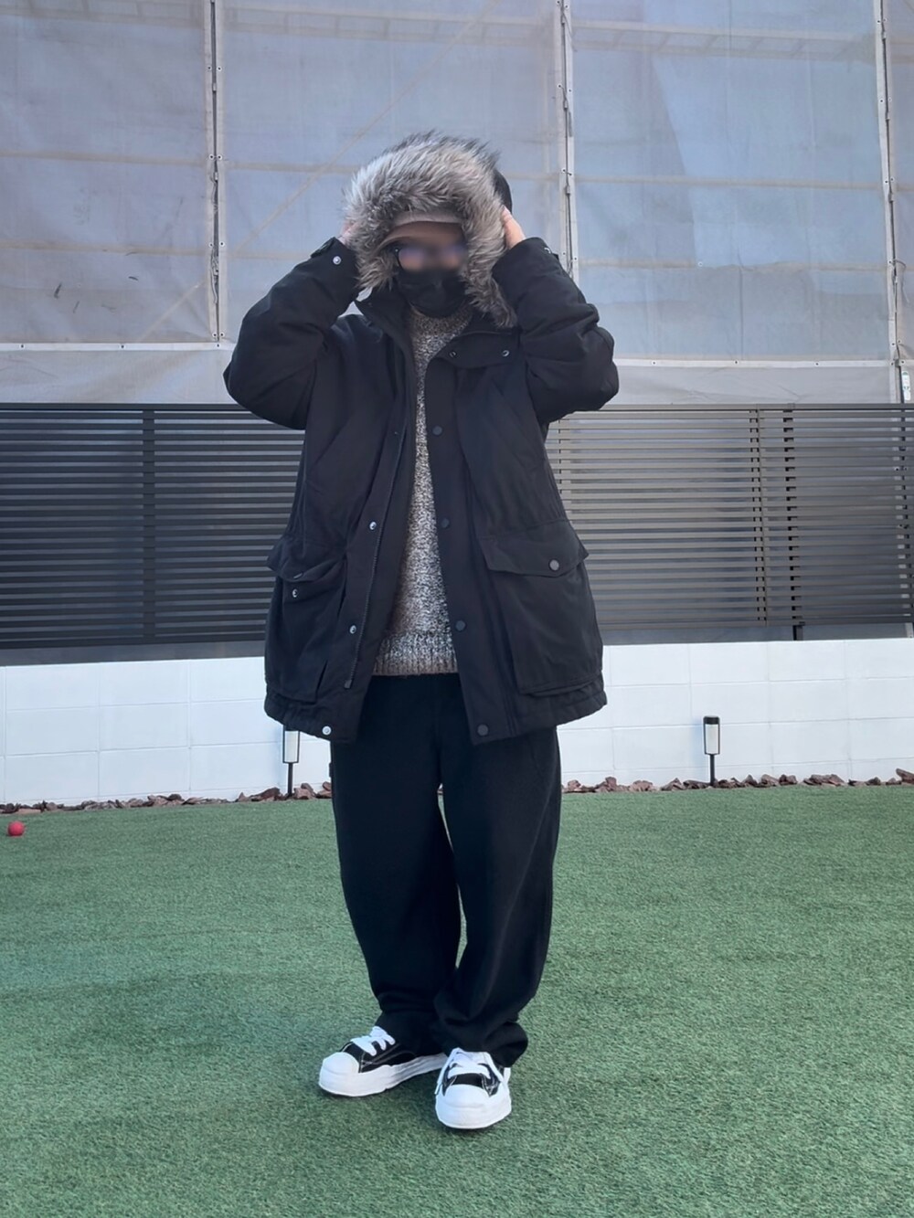 ブラック系のモッズコート、ブラウン系のニット/セーター、ブラック系のスニーカーを着用したメンズの春コーディネートの2枚目の写真