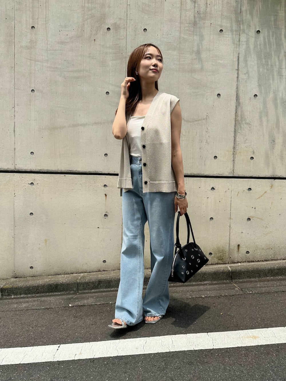 シルバー系のサンダル、ブラック系のボストンバッグ、ホワイト系のベストを着用したレディースの夏コーディネートの2枚目の写真