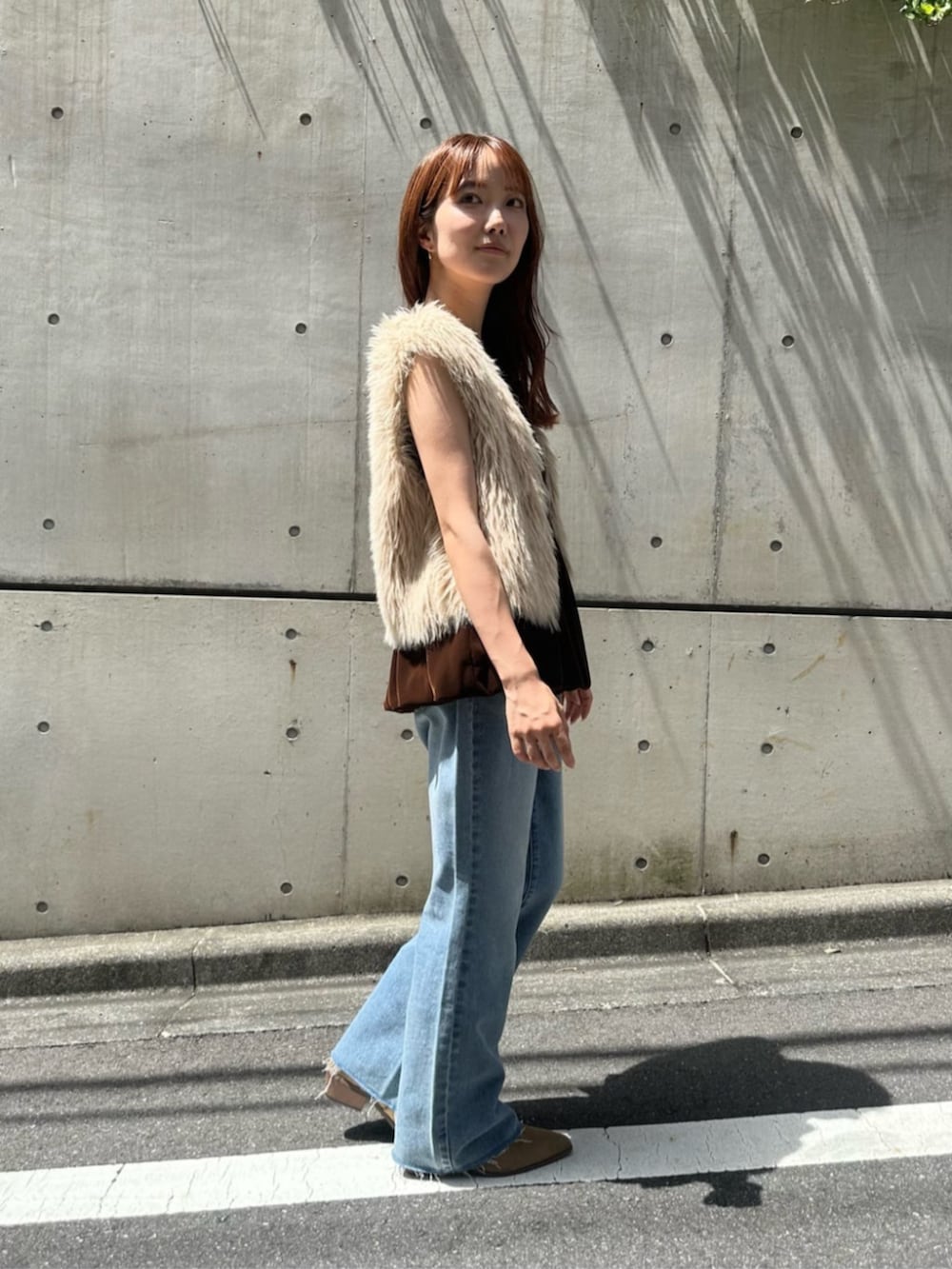 ベージュ系のベスト、ブラウン系のキャミソール、ブルー系のデニムパンツを着用したレディースの秋コーディネートの2枚目の写真