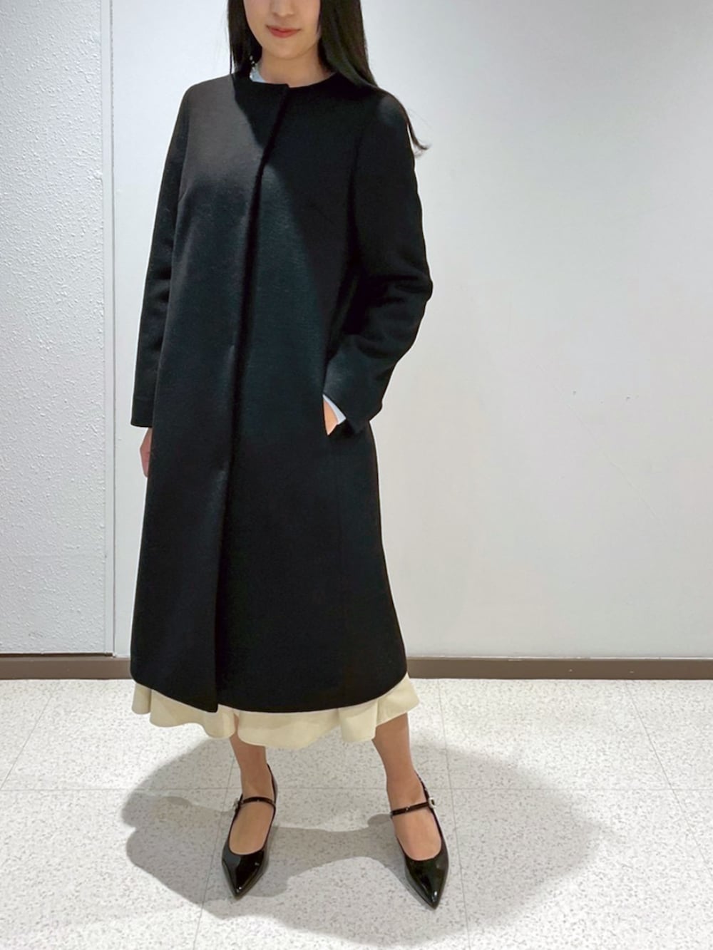 ホワイト系のノーカラーコート、ホワイト系のニット/セーターを着用したレディースの冬コーディネートの2枚目の写真