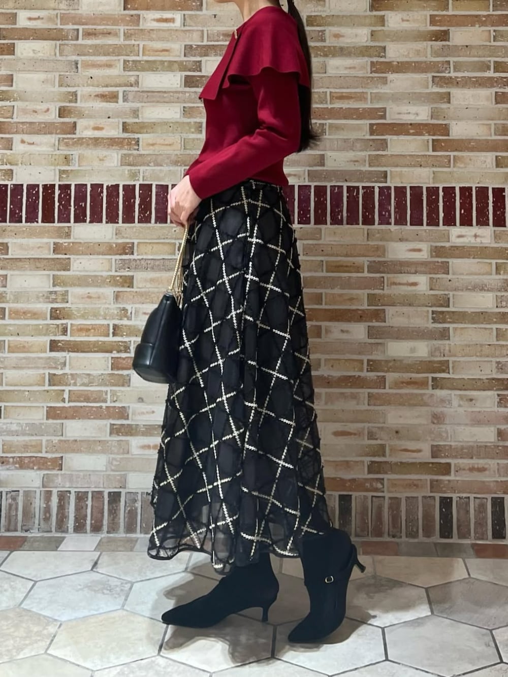 レッド系のニット/セーター、グレー系のスカートを着用したレディースの冬コーディネートの2枚目の写真