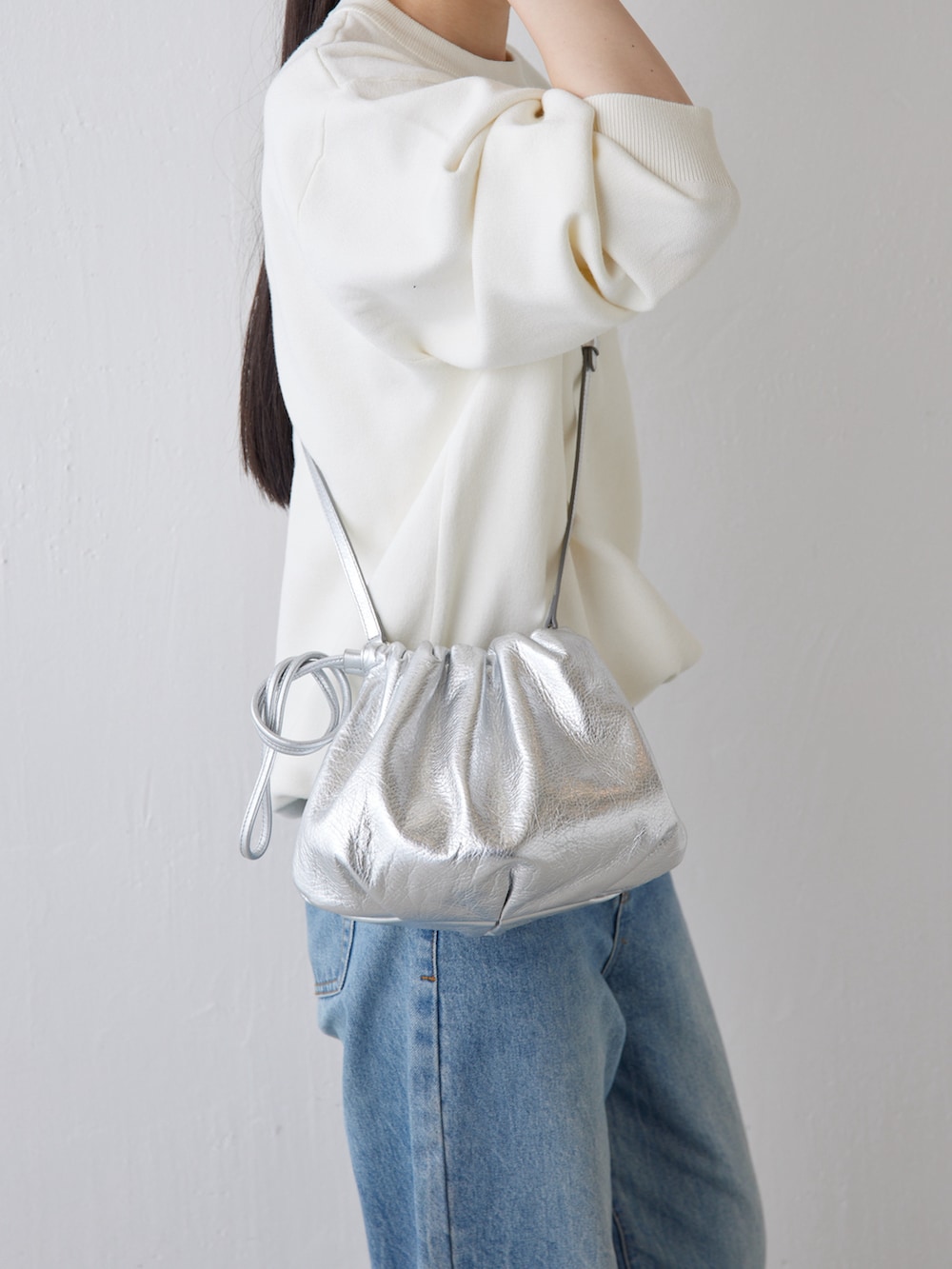 シルバー系のショルダーバッグ、ブルー系のデニムパンツ、ホワイト系のニット/セーターを着用したレディースの秋コーディネートの4枚目の写真