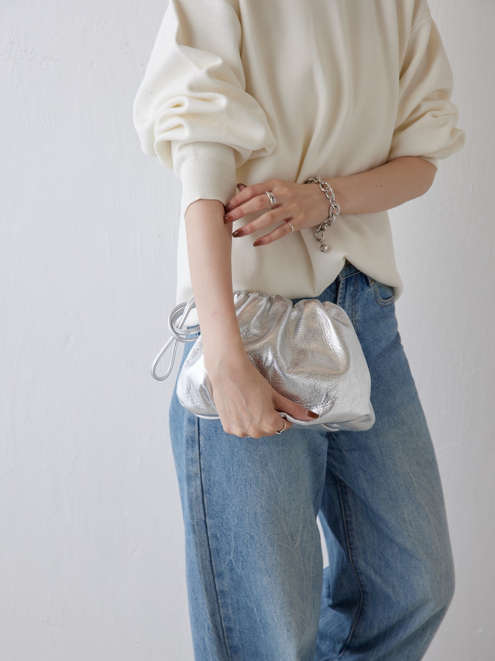 シルバー系のショルダーバッグ、ブルー系のデニムパンツ、ホワイト系のニット/セーターを着用したレディースの秋コーディネートの2枚目の写真