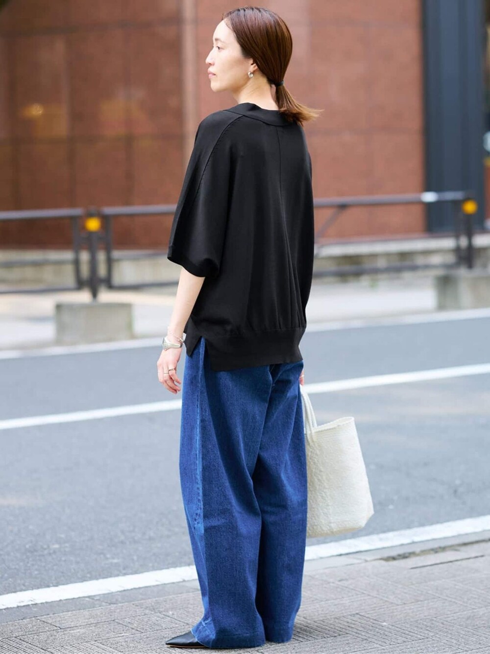 ブルー系のデニムパンツ、ブラック系のニット/セーター、ホワイト系のトートバッグを着用したレディースの夏コーディネートの3枚目の写真