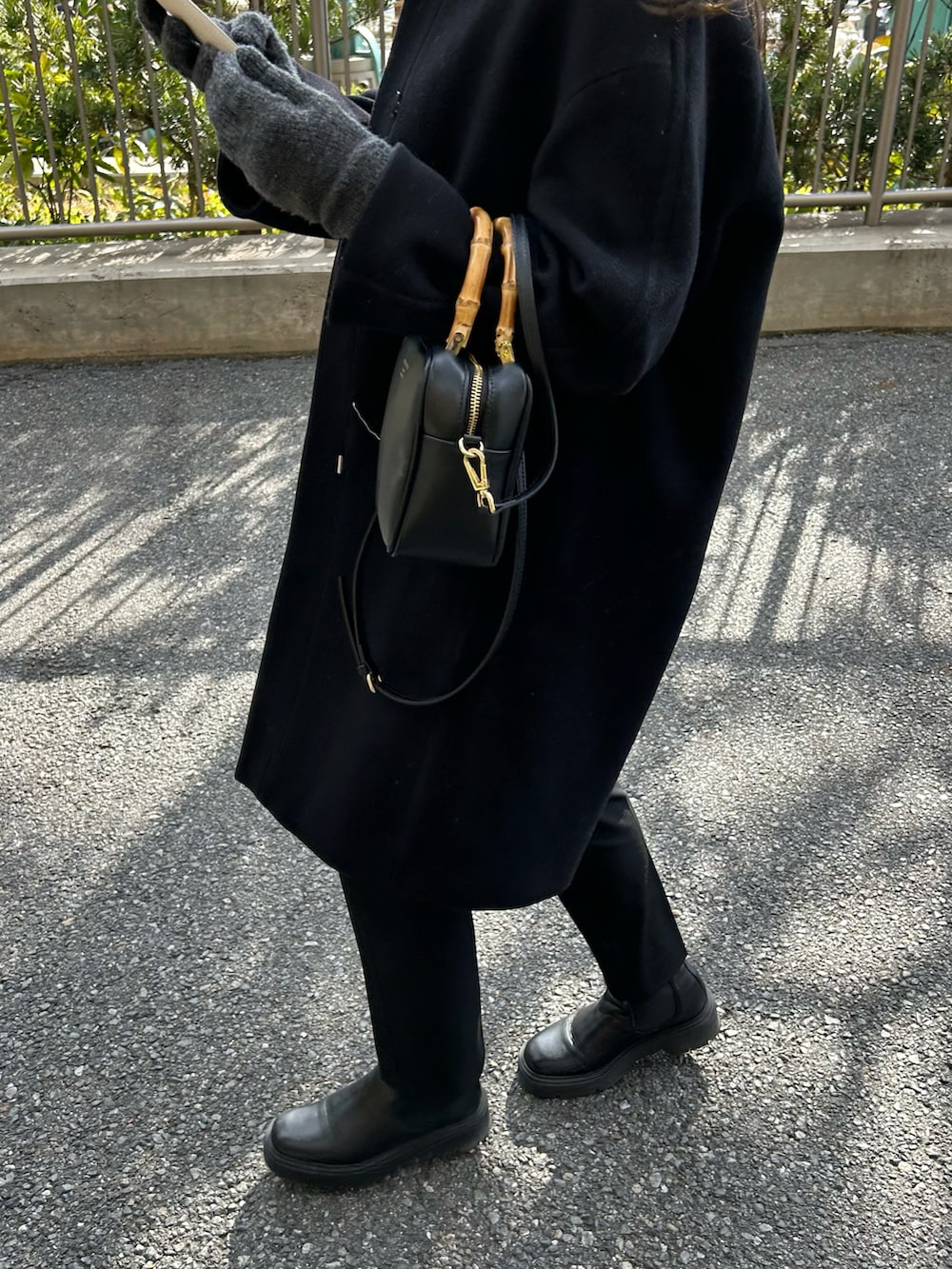 ブラック系のノーカラーコート、ブラック系のショルダーバッグ、グレー系のカーディガン/ボレロを着用したレディースの冬コーディネートの2枚目の写真