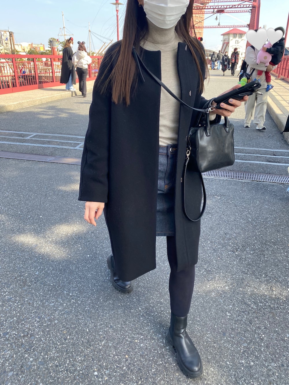 ブラック系のノーカラーコート、ブルー系のデニムスカート、ブラック系のハンドバッグを着用したレディースの冬コーディネートの3枚目の写真