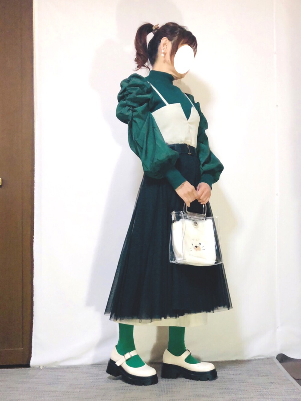 グリーン系のニット/セーター、ホワイト系のジャンパースカート、ブラック系のスカートを着用したレディースの秋コーディネートの2枚目の写真