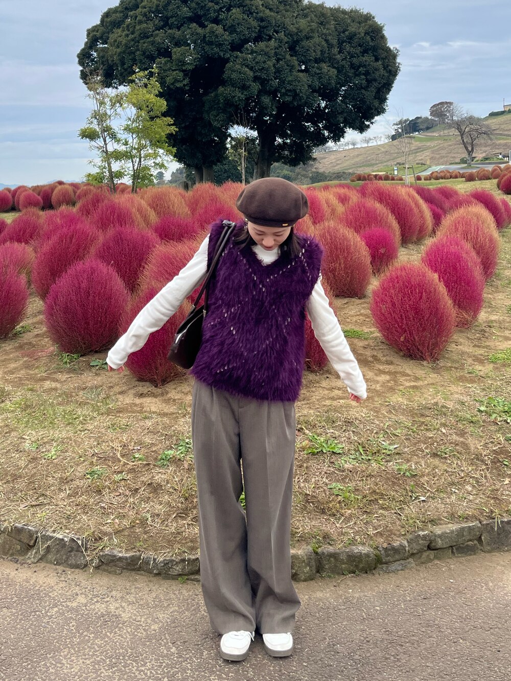 パープル系のベスト、ブラウン系のその他パンツ、レッド系のハンドバッグを着用したレディースの秋コーディネートの2枚目の写真