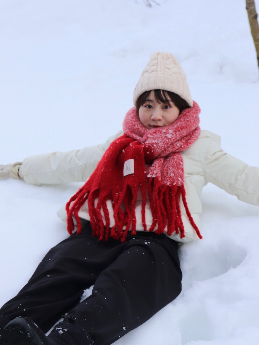 ホワイト系のダウンジャケット/コート、レッド系のマフラー、ホワイト系のニットキャップ/ビーニーを着用したレディースの冬コーディネートの2枚目の写真