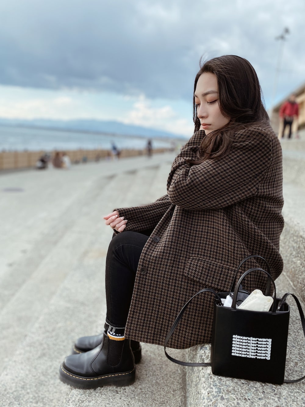 ブラック系のデニムパンツ、ブラック系のブーツ、ブラウン系のチェスターコートを着用したレディースの春コーディネートの2枚目の写真